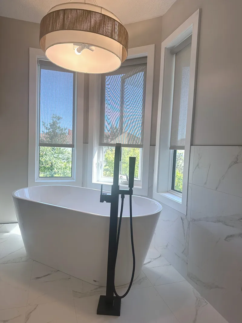 Freestanding bathtub beneath a pendant light and bay windows in McKenzie Towne