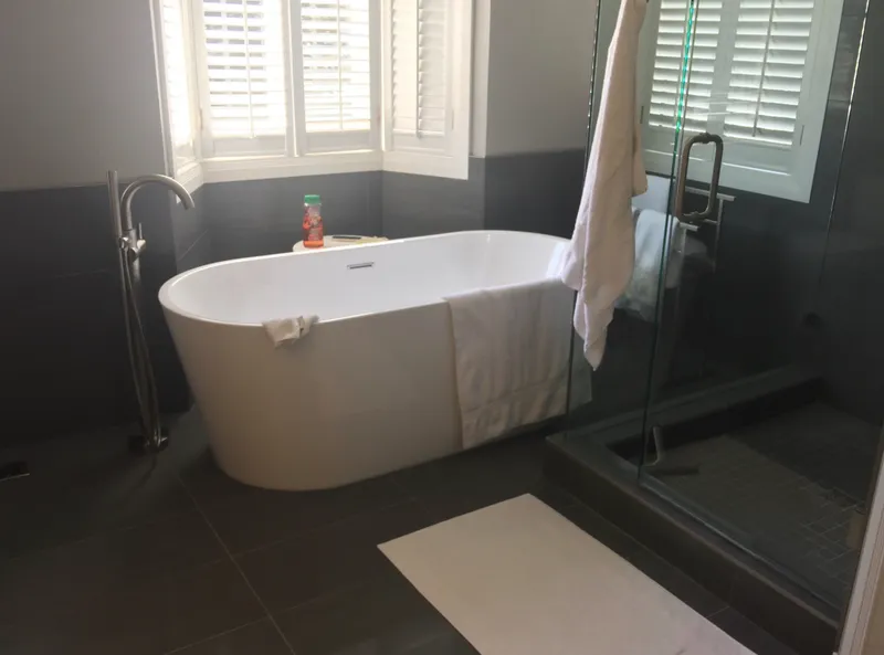 Freestanding bathtub beside a glass shower and shuttered windows