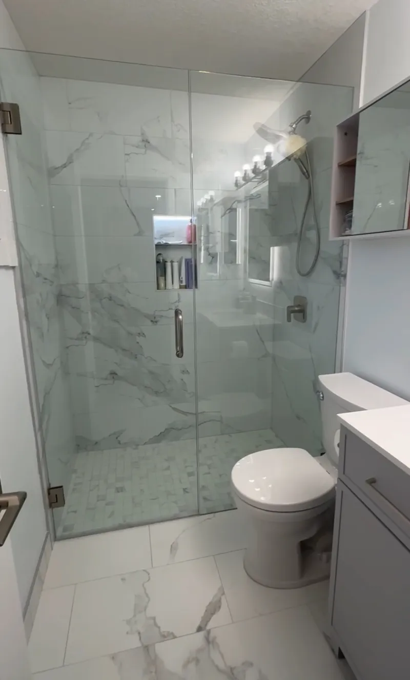 Glass shower and compact bathroom with pale stone-pattern tile