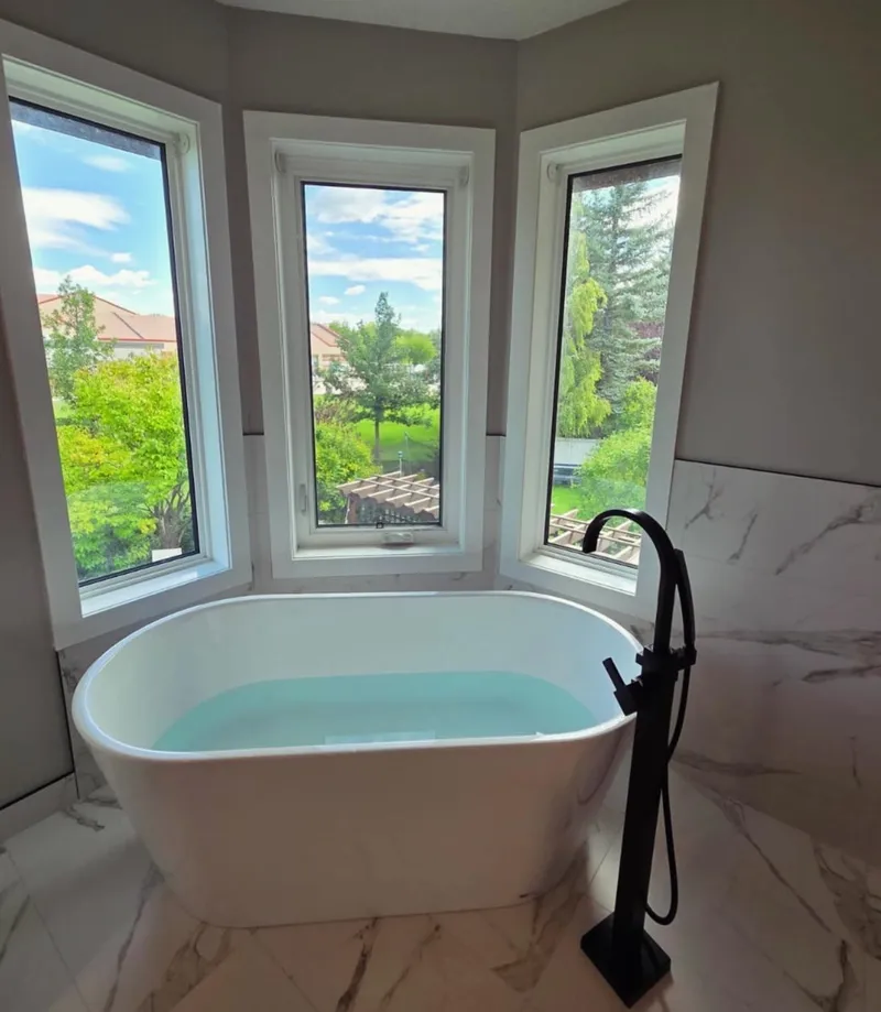 White freestanding bathtub at a bay window with a black floor-mounted tap